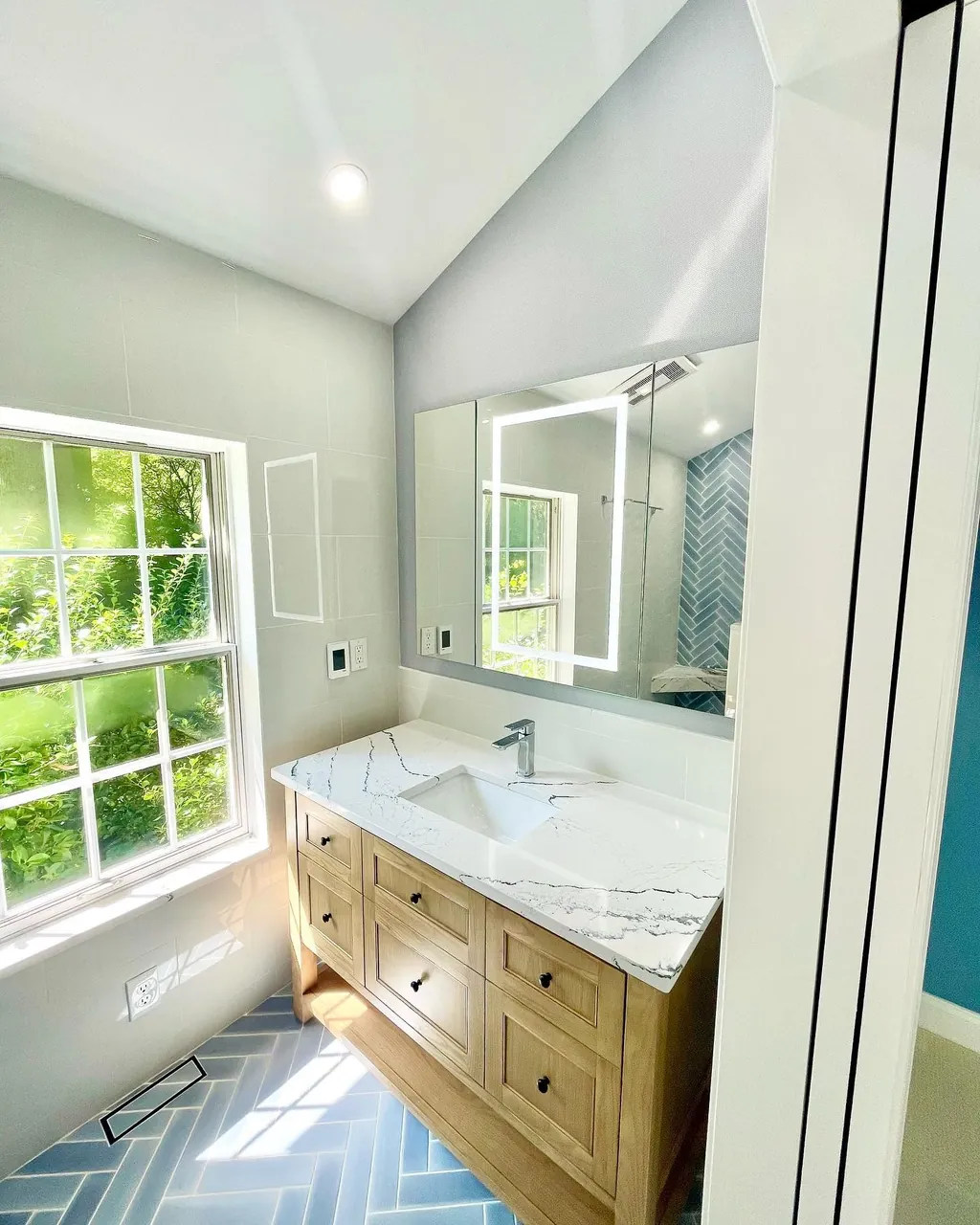 Light-filled bathroom remodel with custom vanity and blue tile floor by Delpa Builders